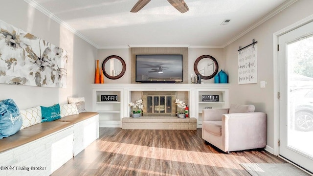 living area featuring crown molding, a fireplace, hardwood / wood-style flooring, and ceiling fan