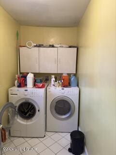 laundry room featuring washing machine and clothes dryer, light tile patterned floors, and cabinets