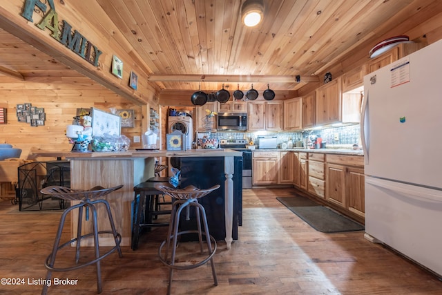 kitchen featuring light brown cabinets, hardwood / wood-style flooring, wooden walls, stainless steel appliances, and a kitchen bar