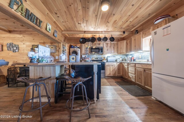kitchen with light brown cabinetry, wood finished floors, a breakfast bar area, light countertops, and stainless steel appliances