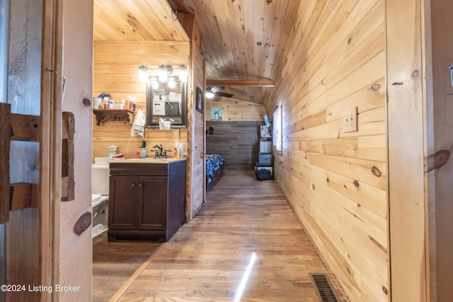 hall with visible vents, wood finished floors, wooden walls, wooden ceiling, and a sink