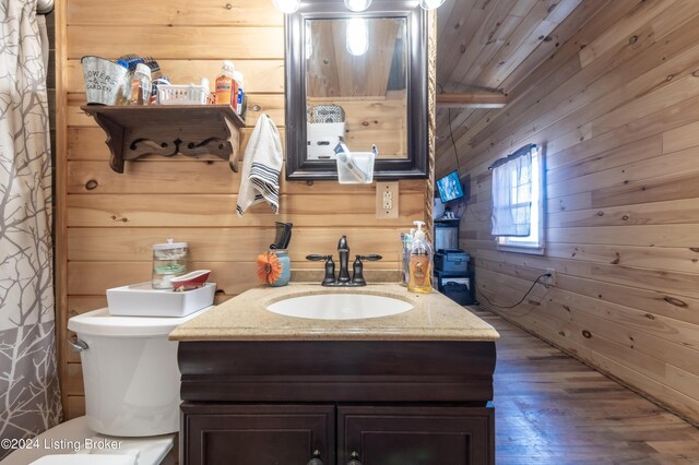bathroom featuring wooden walls, toilet, wood finished floors, and vanity