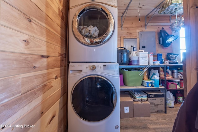 clothes washing area with laundry area, stacked washer and dryer, wood finished floors, and wood walls