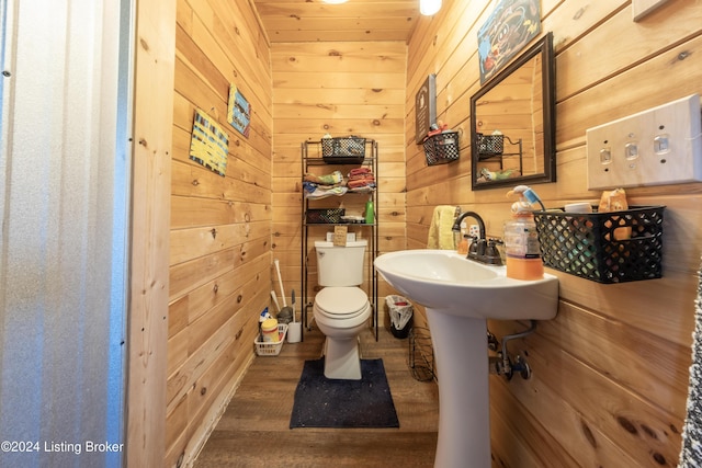 half bath featuring wooden walls, toilet, a sink, and wood finished floors