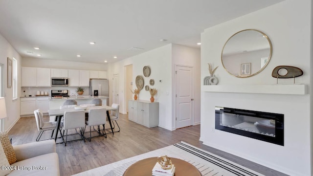 kitchen with light hardwood / wood-style flooring, white cabinetry, stainless steel appliances, and a breakfast bar area