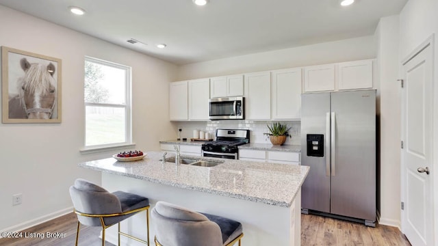 kitchen featuring tasteful backsplash, appliances with stainless steel finishes, light wood-type flooring, white cabinets, and a center island with sink