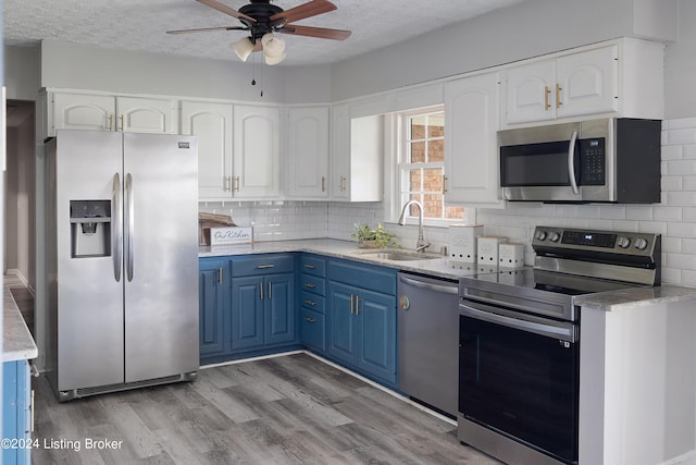 kitchen with stainless steel appliances, sink, blue cabinetry, white cabinets, and a textured ceiling