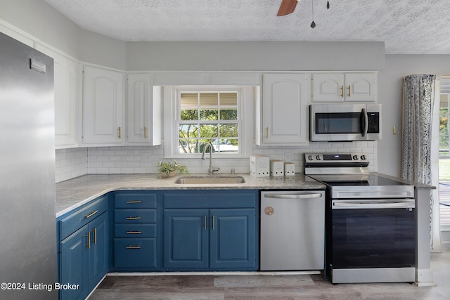 kitchen featuring appliances with stainless steel finishes, sink, light wood-type flooring, white cabinets, and blue cabinetry