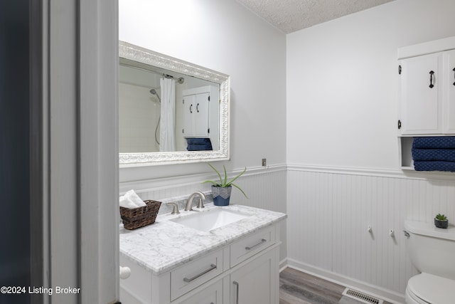 bathroom with a textured ceiling, wood-type flooring, toilet, vanity, and a shower with curtain