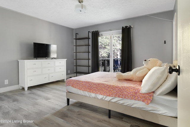 bedroom with light hardwood / wood-style floors, access to outside, and a textured ceiling