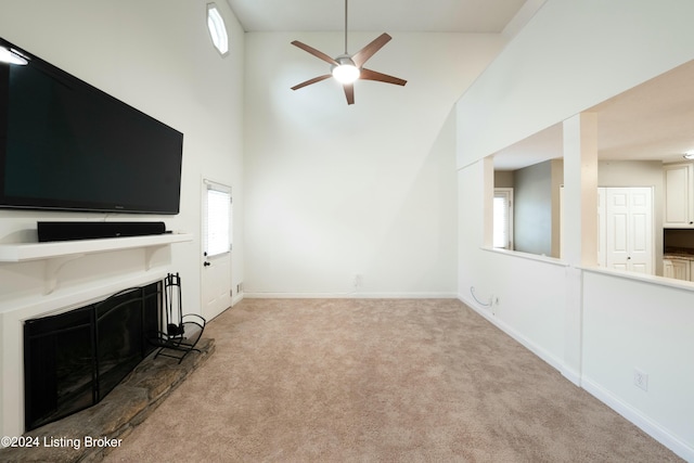 unfurnished living room featuring ceiling fan, a fireplace, a high ceiling, and light carpet