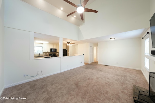 unfurnished living room featuring ceiling fan, sink, a towering ceiling, and light colored carpet