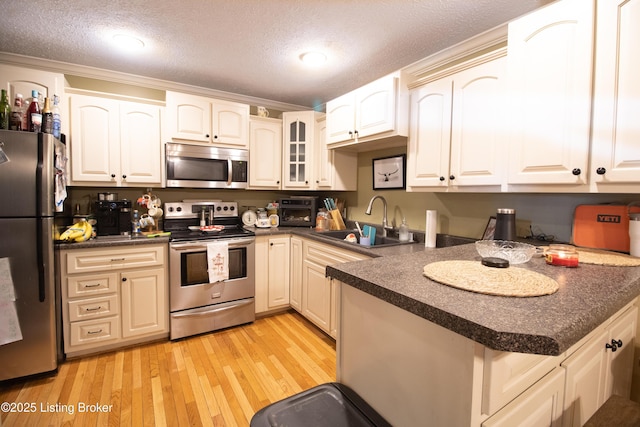 kitchen with a peninsula, a sink, appliances with stainless steel finishes, dark countertops, and glass insert cabinets