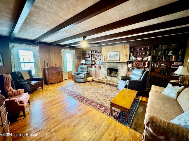 living room featuring beam ceiling, built in shelves, light hardwood / wood-style flooring, and a fireplace