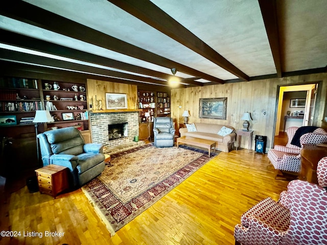 living room featuring wood walls, beamed ceiling, wood-type flooring, and a fireplace