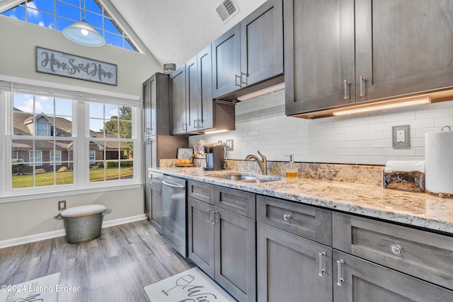 kitchen with light stone countertops, sink, light wood-type flooring, lofted ceiling, and stainless steel dishwasher