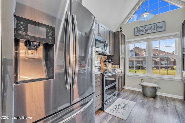 kitchen with appliances with stainless steel finishes, light hardwood / wood-style flooring, and vaulted ceiling