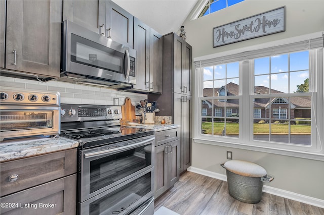 kitchen featuring appliances with stainless steel finishes, dark brown cabinetry, lofted ceiling, light stone counters, and light hardwood / wood-style flooring