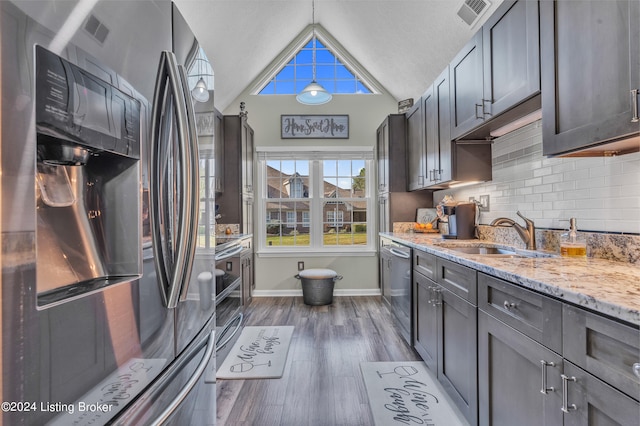 kitchen with appliances with stainless steel finishes, sink, vaulted ceiling, light stone counters, and dark hardwood / wood-style floors