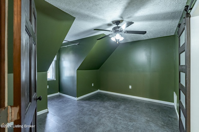 additional living space featuring ceiling fan, a textured ceiling, lofted ceiling, and a barn door