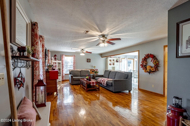 living room featuring a textured ceiling, light wood-type flooring, and ceiling fan