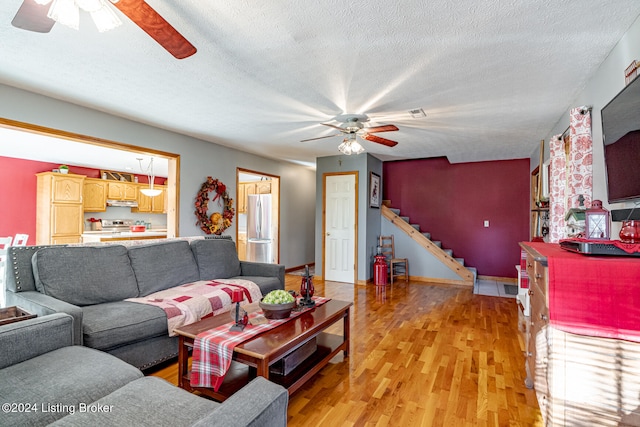 living room with ceiling fan, a textured ceiling, and light wood-type flooring