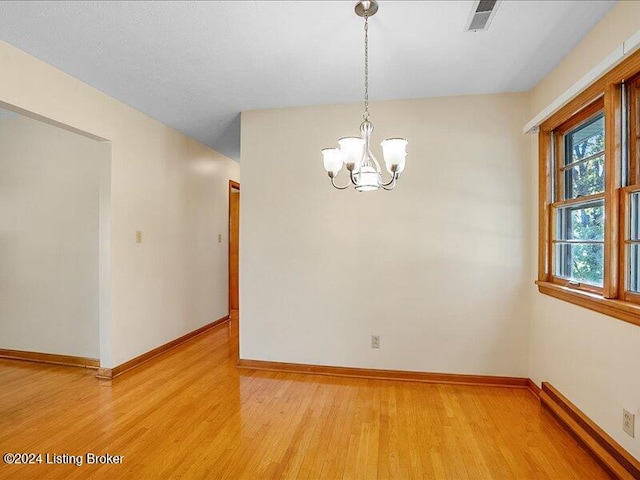 empty room with a notable chandelier, hardwood / wood-style floors, and a baseboard heating unit