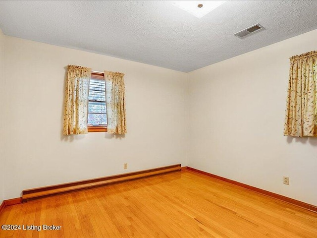 empty room featuring hardwood / wood-style flooring, a textured ceiling, and a baseboard heating unit