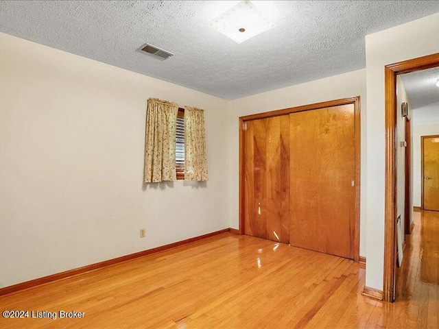 unfurnished bedroom with light hardwood / wood-style floors, a closet, and a textured ceiling