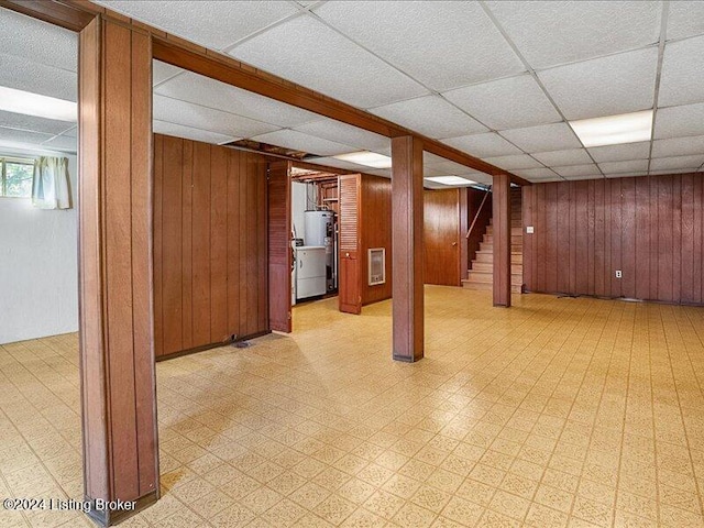 basement with wooden walls, water heater, and a paneled ceiling