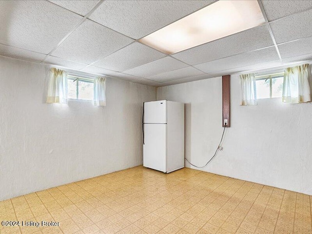 basement featuring a drop ceiling and white refrigerator