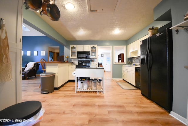 kitchen with light hardwood / wood-style flooring, black appliances, a textured ceiling, and white cabinets