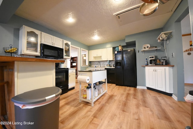 kitchen featuring black appliances, light wood-type flooring, decorative backsplash, and white cabinets