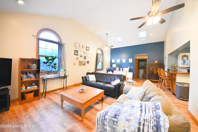 living room featuring ceiling fan, vaulted ceiling with skylight, and light hardwood / wood-style flooring