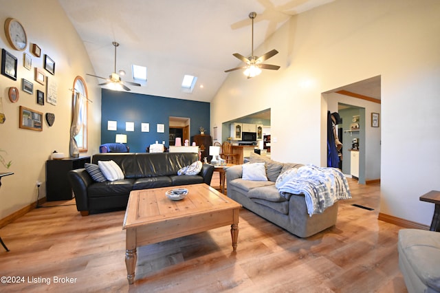 living room with light hardwood / wood-style flooring, high vaulted ceiling, a skylight, and ceiling fan