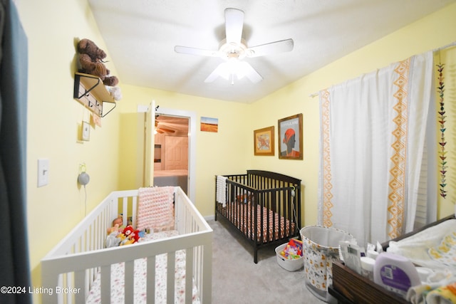 bedroom featuring a nursery area, light colored carpet, and ceiling fan