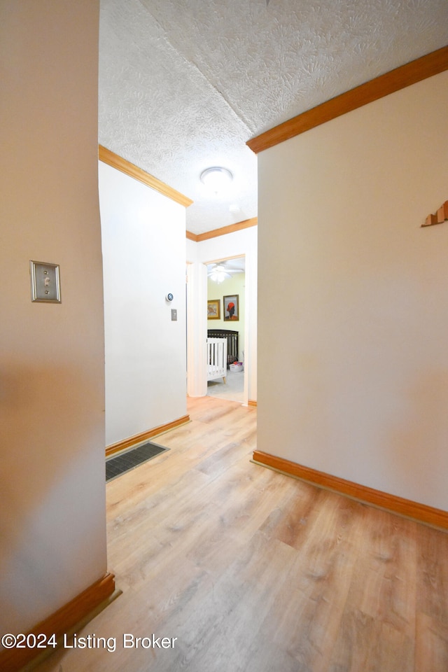 hallway with a textured ceiling, ornamental molding, light wood-type flooring, and radiator heating unit