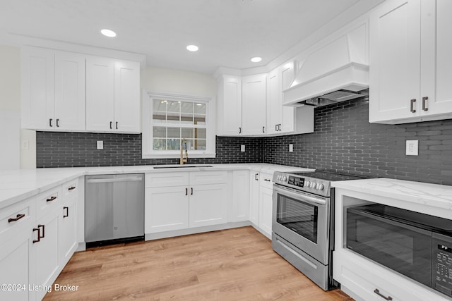 kitchen featuring stainless steel appliances, sink, white cabinets, custom exhaust hood, and light hardwood / wood-style flooring