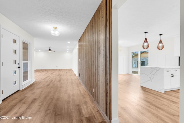 hallway featuring wood walls, light wood-type flooring, and a textured ceiling