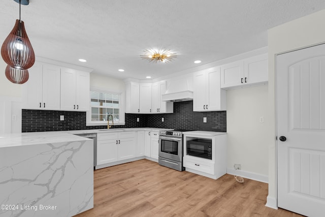 kitchen featuring appliances with stainless steel finishes, decorative light fixtures, custom range hood, and light hardwood / wood-style floors