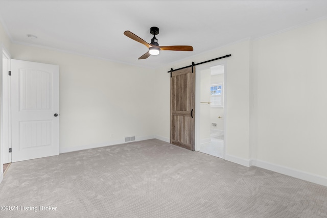 unfurnished bedroom with ornamental molding, a barn door, light colored carpet, ceiling fan, and ensuite bathroom