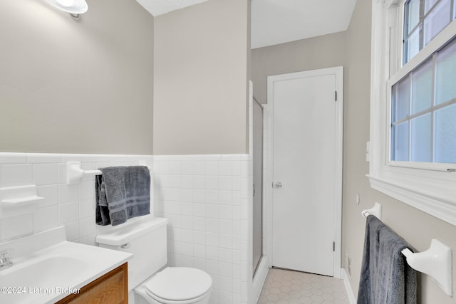 bathroom with tile patterned floors, toilet, vanity, tile walls, and an enclosed shower