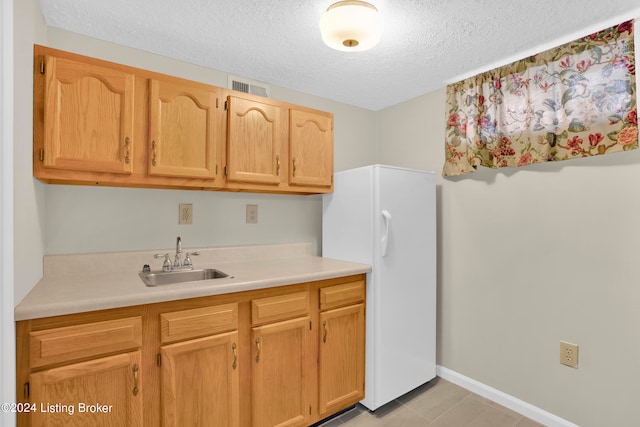 kitchen featuring light tile patterned floors, a textured ceiling, sink, and white refrigerator