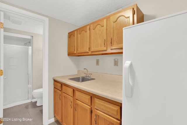 kitchen with light tile patterned floors, white fridge with ice dispenser, a textured ceiling, and sink