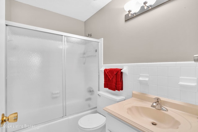 full bathroom featuring vanity, tile walls, combined bath / shower with glass door, and toilet