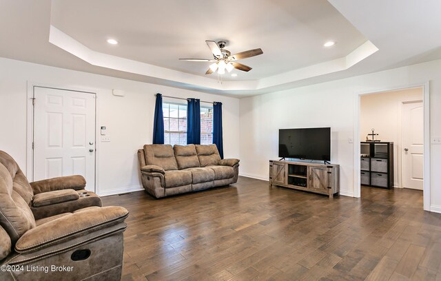 living room with ceiling fan, a raised ceiling, and dark hardwood / wood-style floors