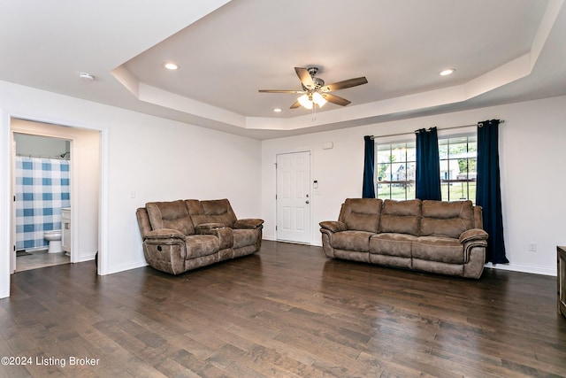 living room with dark hardwood / wood-style floors, a tray ceiling, and ceiling fan