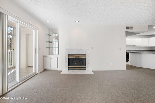 unfurnished living room featuring a premium fireplace, light carpet, and a textured ceiling