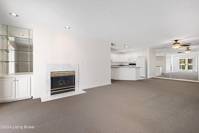 unfurnished living room with a textured ceiling, carpet floors, and ceiling fan