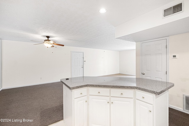 kitchen with a textured ceiling, a kitchen island, dark colored carpet, and white cabinets